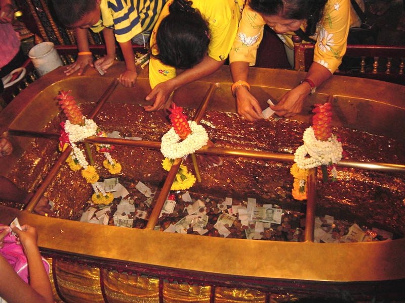 仏足石の内側に金箔を貼り、お金をその中へタンブン（喜捨）して祈りを捧げる人たち