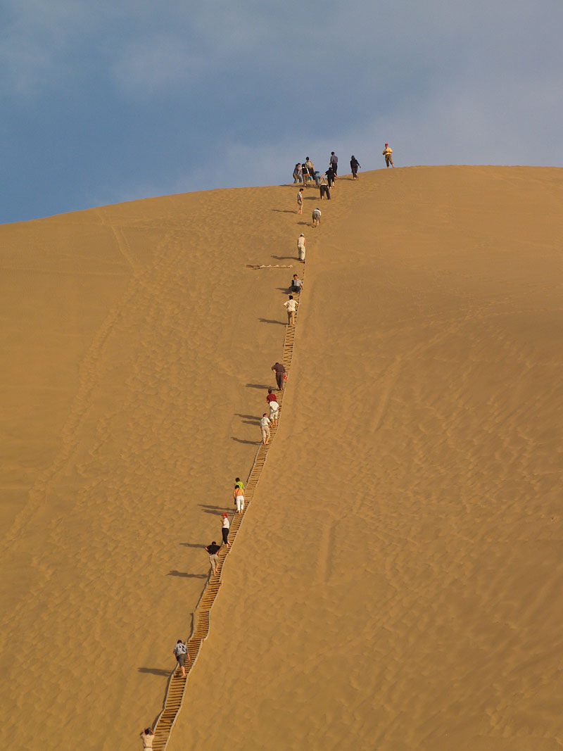 裸足で砂山を登る人たち